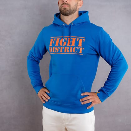 Photo de face d'un homme portant un hoodie bleu au logo orange de la collection The Original