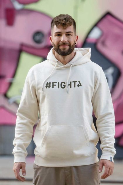 Un homme portant le Hoodie couleur blanc crème avec le logo "#Fight4"