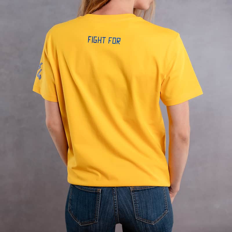 Image de dos d'une femme portant un T-Shirt jaune au logo bleu de la collection Cabal Skull