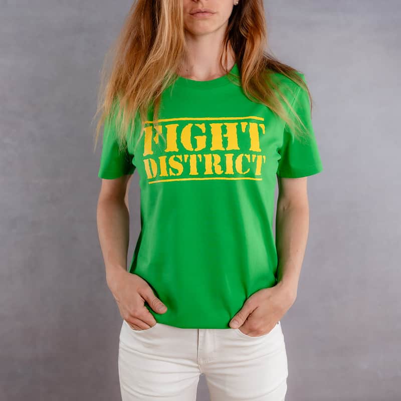 Photo de face d'une femme portant un T-shirt vert au logo jaune de la collection The Original