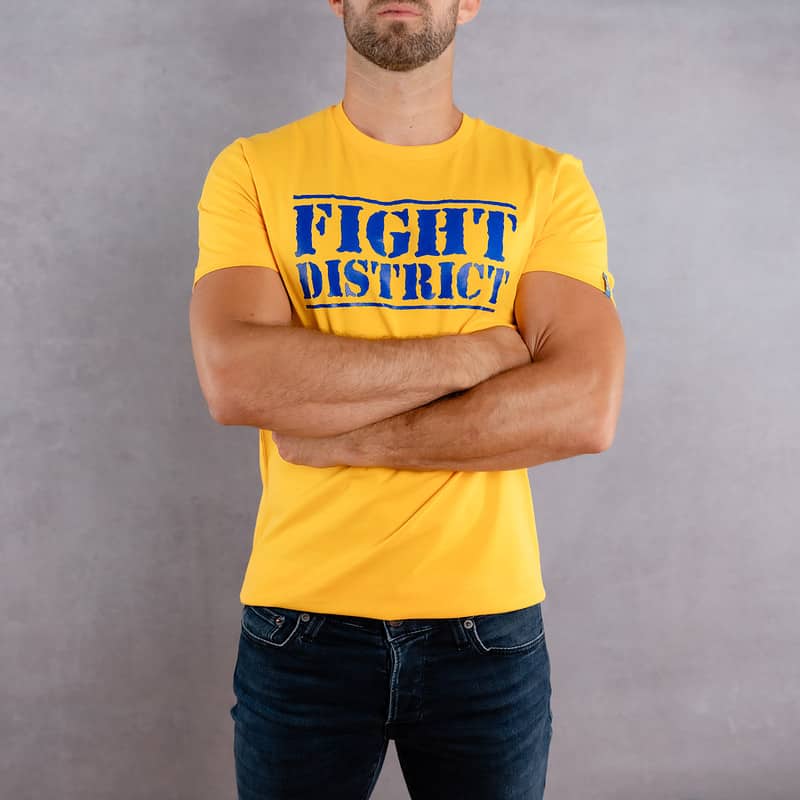 Image de face d'un homme portant un T-Shirt jaune au logo bleu de la collection The Original