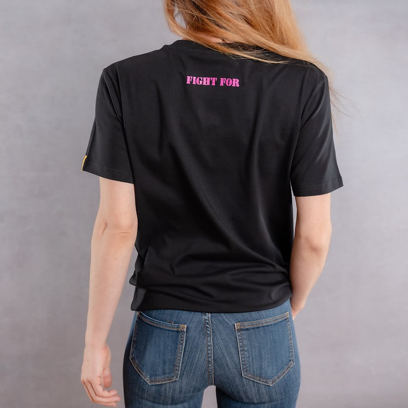 Photo de dos d'une femme portant un T-shirt noir au logo rose de la collection The Original