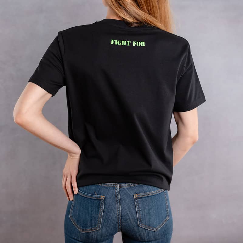 Photo de dos d'une femme portant un T-shirt noir au logo vert de la collection The Original