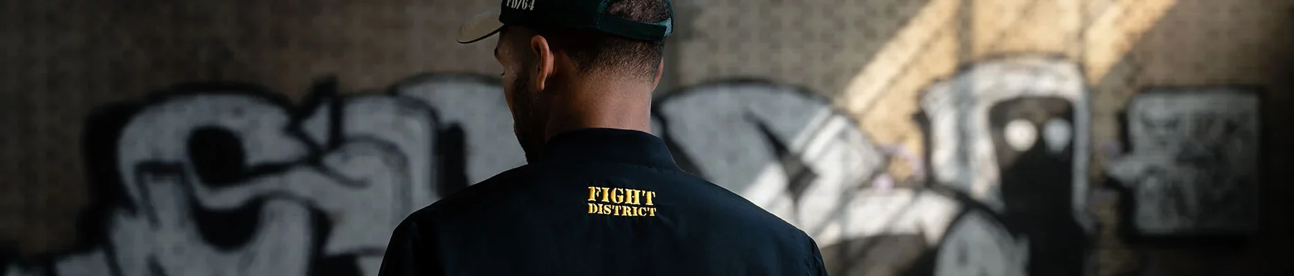 Un homme de dos, on peut voir sur sa veste et sa casquette le logo de Fight District